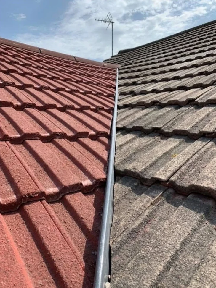 Metal flashing at the junction between red and weathered pitched roof tiles