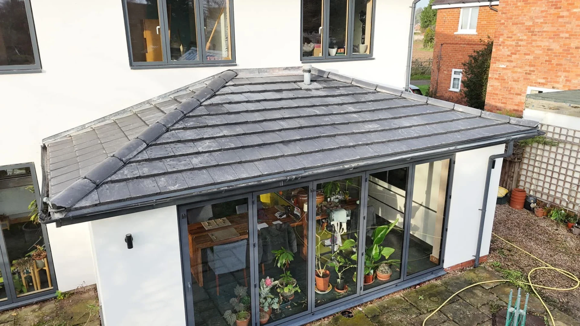 Black gutter run and downpipe around a grey tiled extension roof