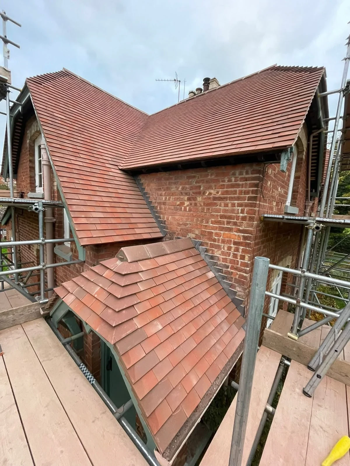 Red tiled pitched roof and lower canopy roof on a scaffolded brick house