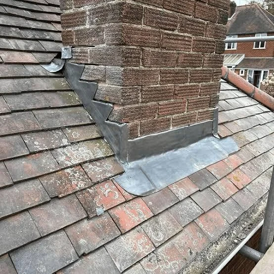 Repointed brick chimney and lead flashing at the tiled roof junction