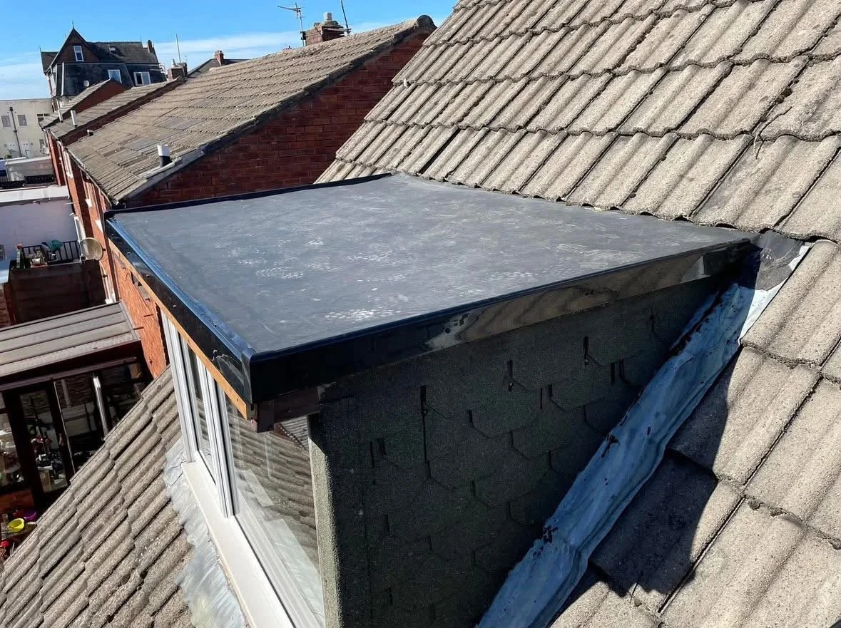 Dark flat roof covering on a small dormer beside weathered concrete roof tiles
