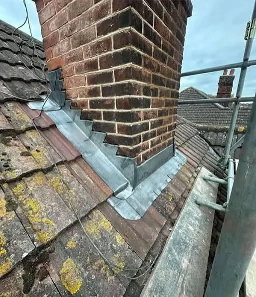 Brick chimney with stepped lead flashing above weathered roof tiles