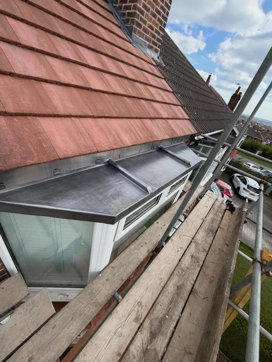 Lead flashing and apron detailing at a tiled roof edge above guttering