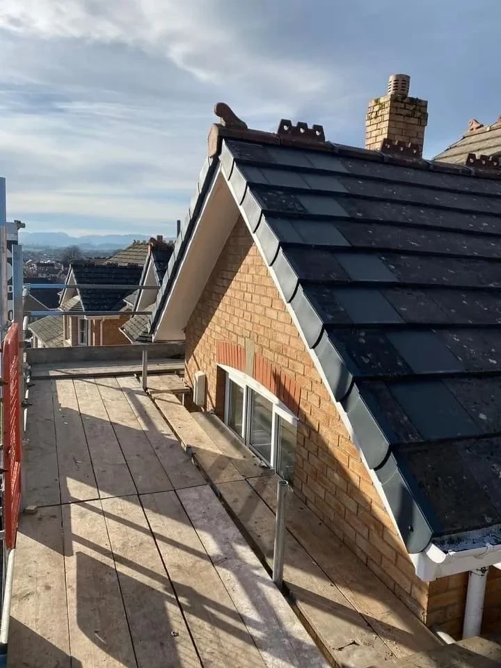 Dark tiles fitted to a brick gable roof with scaffolding alongside
