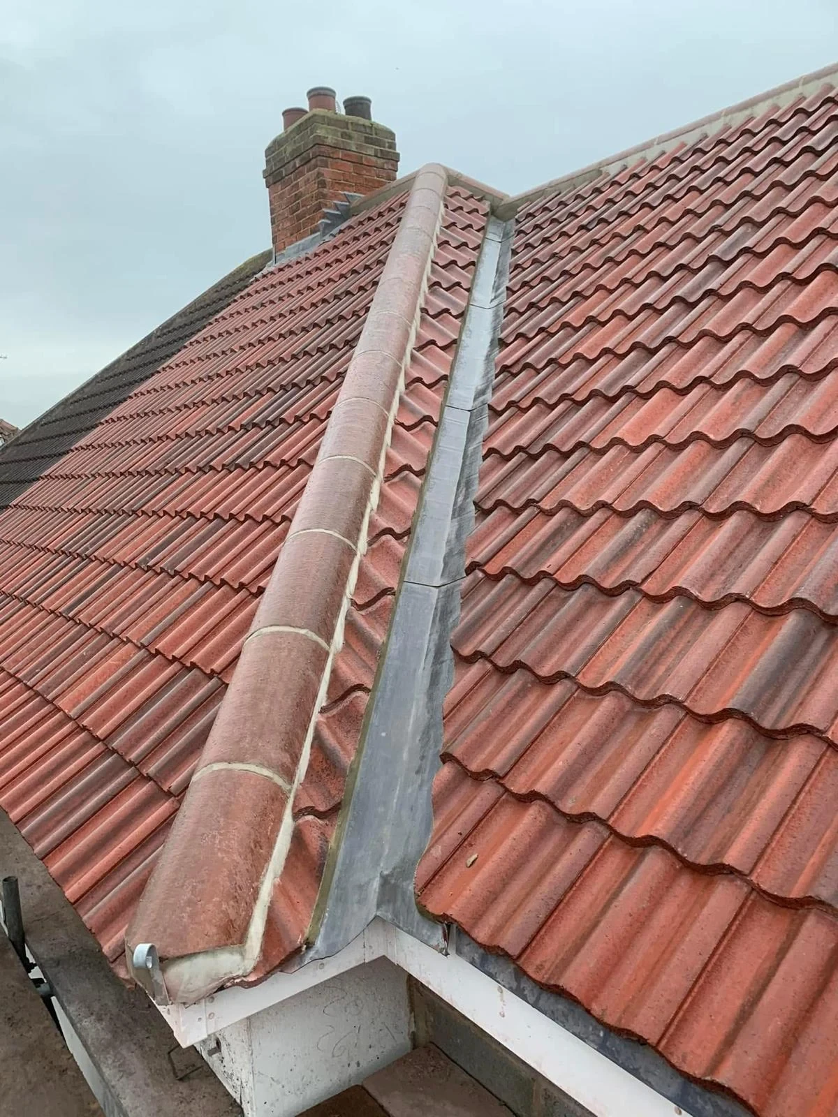 Lead-lined channel beside a raised tiled roof hip with a brick chimney beyond