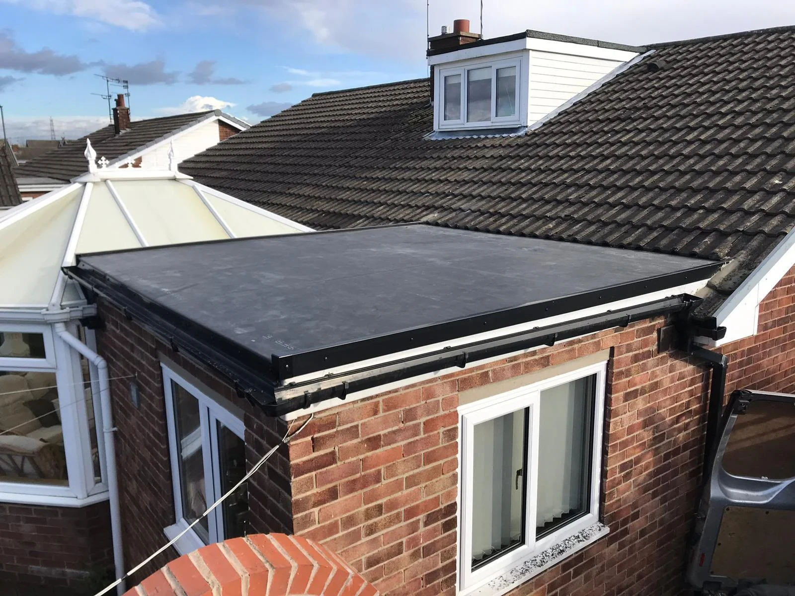 Dark flat roof over a brick extension beside a pitched tiled roof