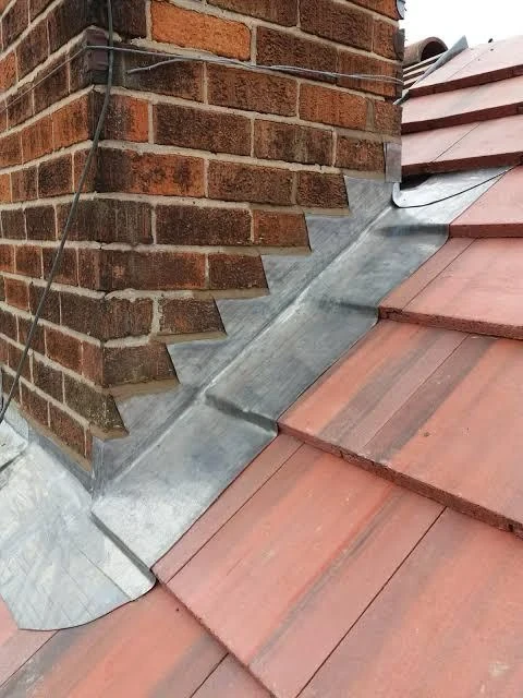 Lead apron and stepped flashing around a brick chimney on red roof tiles