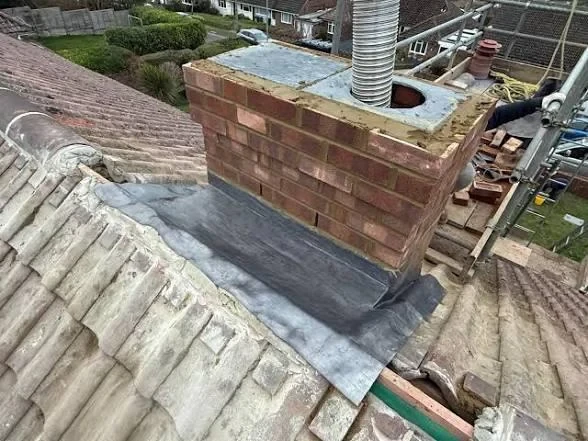 Low brick chimney with metal flue and lead flashing on an older tiled roof