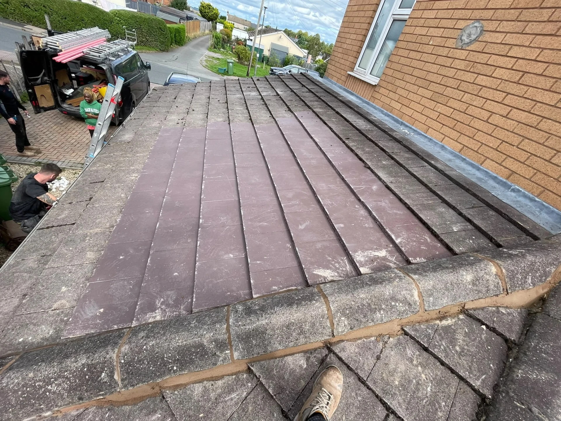 Tiled lower roof beside a brick wall during roof repair work