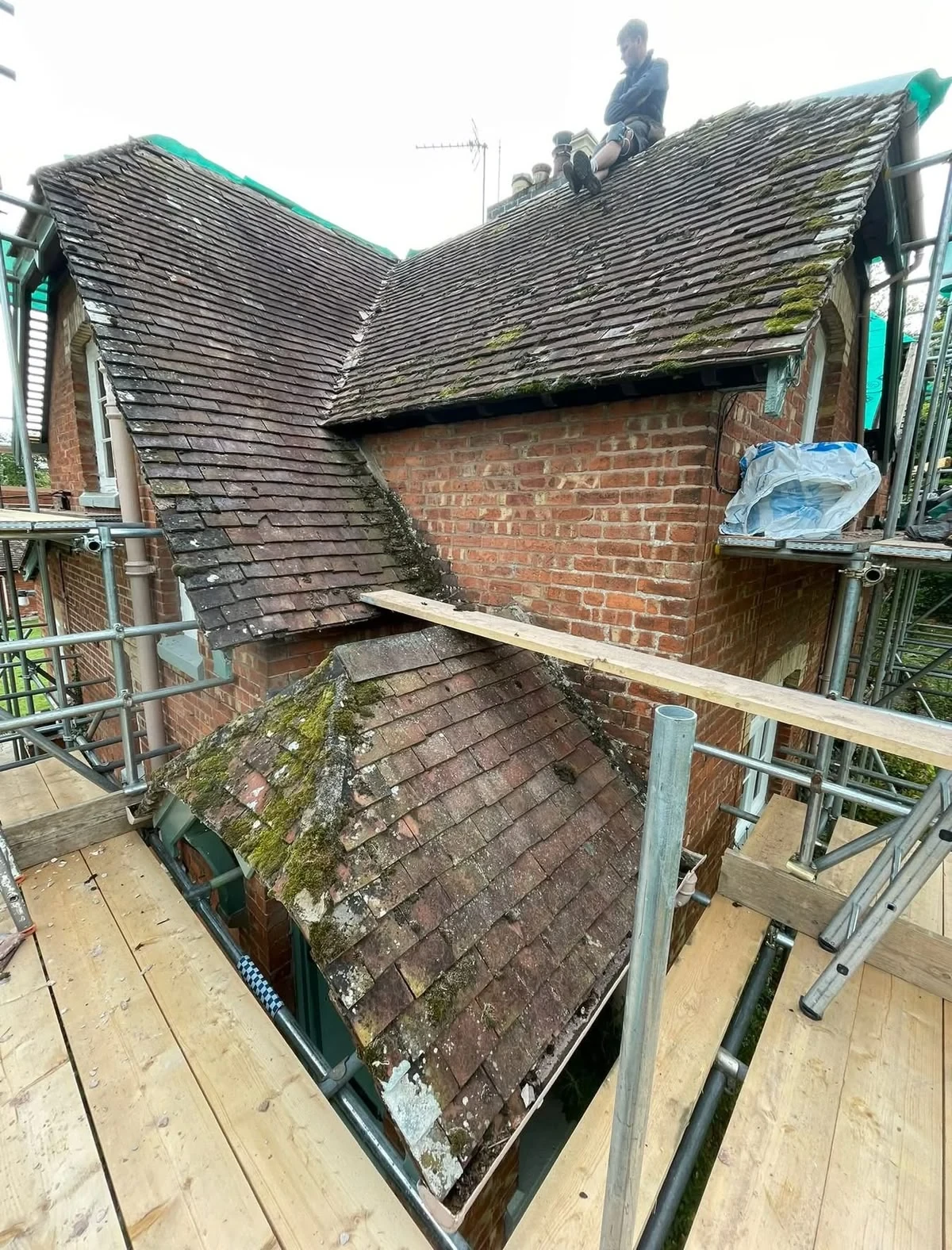 Weathered pitched roof on a brick property with scaffolding before replacement