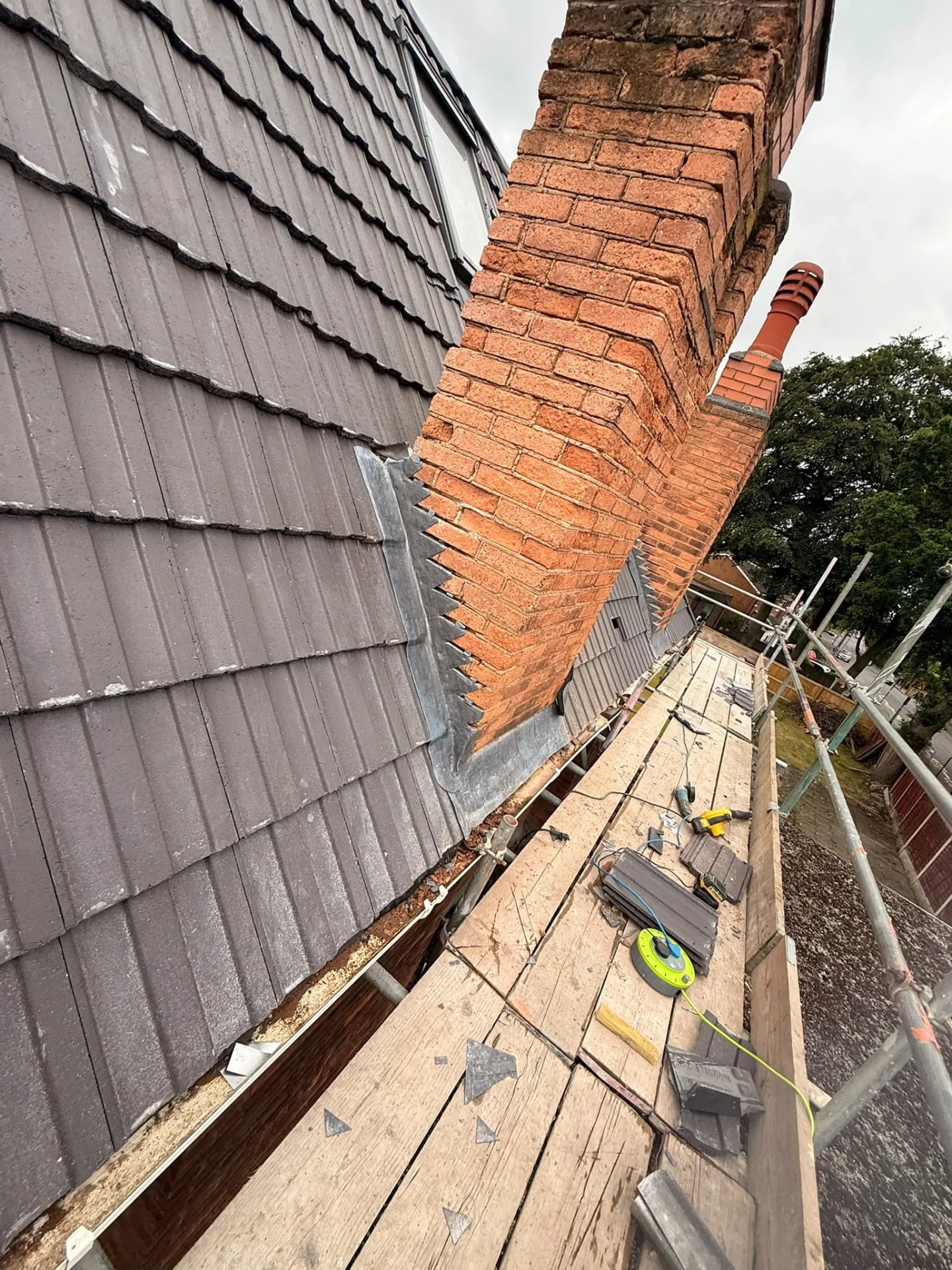 Brick chimney alongside a tiled roof with scaffolding below