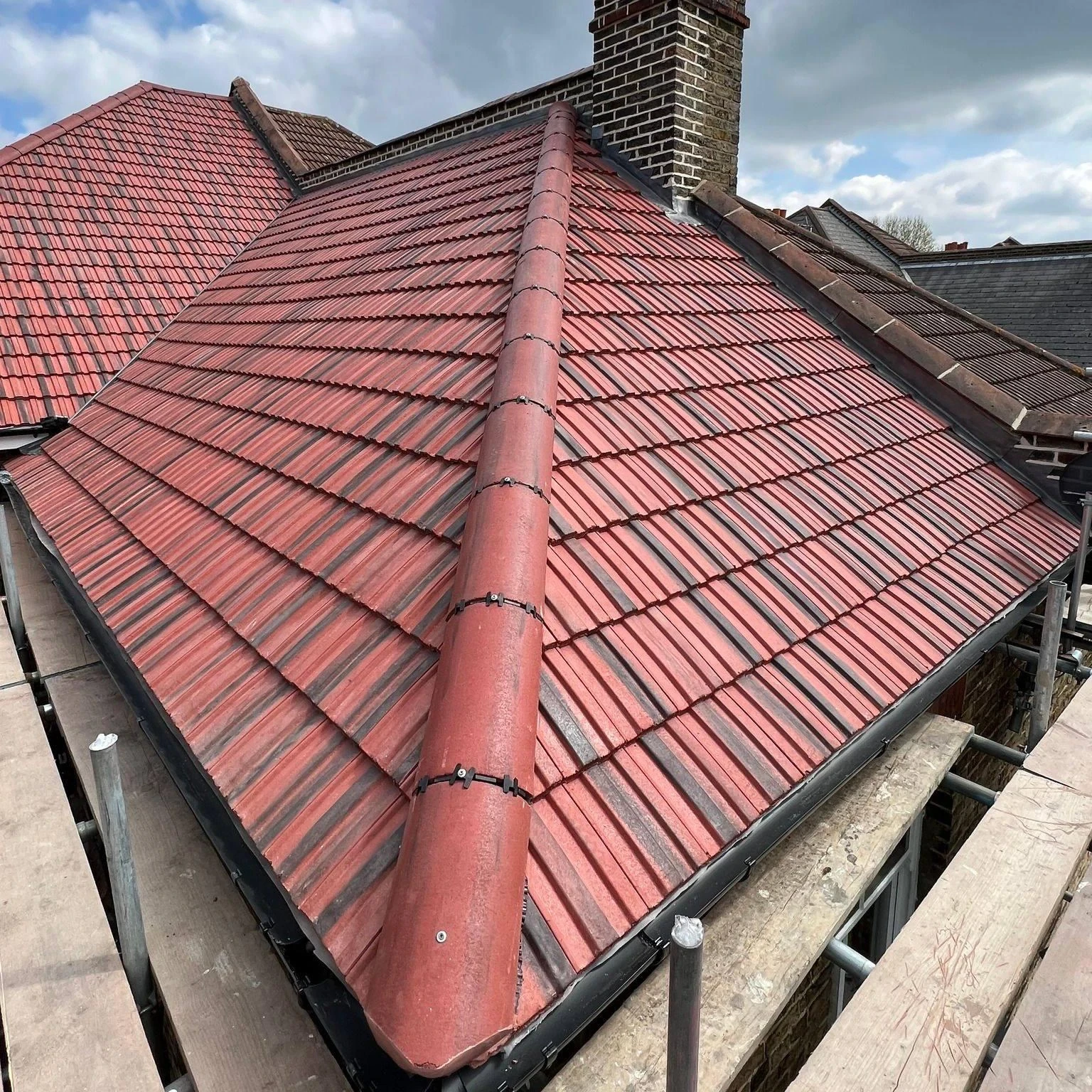 Red tiled roof with mechanically secured hip ridge tiles and black guttering